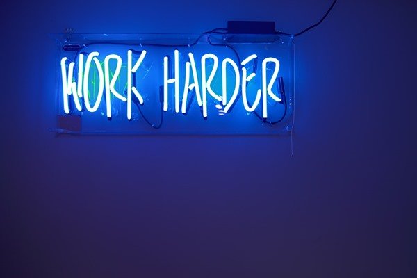 Work harder sign on a wall in neon lights