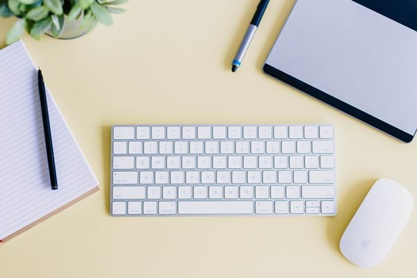 Keyboard, notebook and a pencil on a bright yellow table