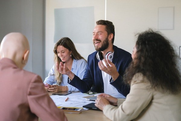 Man talking and explaining something in meeting while smiling and his colleagues listening carefully