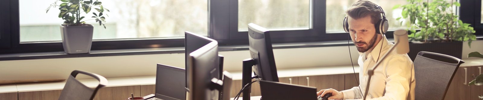 Man with headphones in a white shirt concentrated at work at his desk while working on a computer