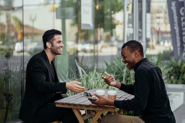 Two colleagues talking over a wooden table with coffee outside the glass office building